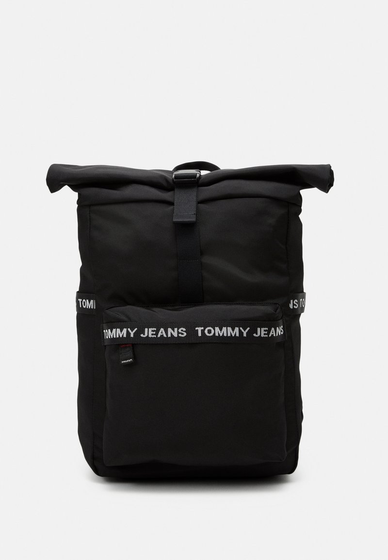 Sac à dos noir à enroulement supérieur avec poche zippée à l'avant et bretelles portant la marque « Tommy Jeans » sur la poche et les côtés, sur fond uni.