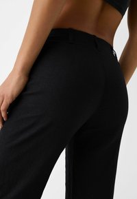 Black linen trousers with a smooth texture, straight-leg design, and side pockets. Features a subtle rear accent near the waistband.