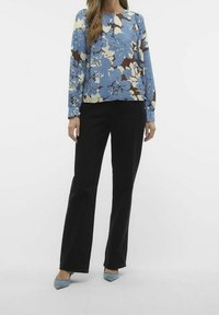 Blumenbluse in Blau, Braun und Creme, mit langen Ärmeln, rundem Ausschnitt, kombiniert mit schwarzen, hell ausgestellten Hosen und hellblauen spitzen Schuhen.