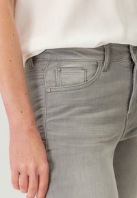 Šedé džíny z denimu s přiléhavým střihem, které mají přední kapsu, zapínání na zip a jemné vyblednutí. Měkká textura s kontrastním šitím.