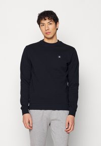 Zwarte crewneck sweatshirt van katoen, met lange mouwen en een klein logo op de borst. Gecombineerd met grijze sweats.