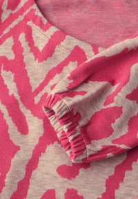 Lichtbeige stof met een roze abstract patroon. Kenmerken zijn een ronde hals en een design met gather aan de mouwboorden. Zachte textuur, casual stijl.