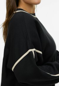 Czarna bluza z kremowym akcentem wzdłuż ramion i rękawów; wykonana z miękkiej, teksturowanej tkaniny, o luźnym kroju.