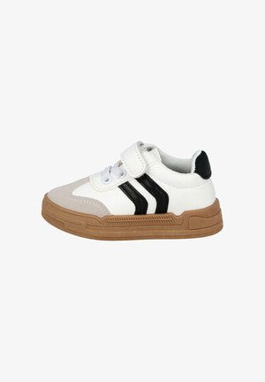 Zapatilla blanca con rayas negras, suela de goma, correa de Velcro y diseño con cordones. Presenta una superficie texturizada y punta redondeada.