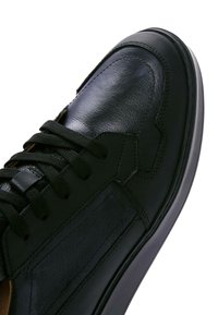 Baskets en cuir noir avec une texture lisse, bout arrondi, accents cousus et semelle en caoutchouc, avec des lacets noirs et des détails sur le panneau latéral.
