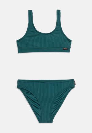 Bañador de dos piezas acanalado en color azul verdoso, con top deportivo de cuello redondo y braguitas de bikini de talle medio a juego sobre fondo blanco.