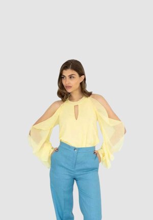 Blusa giallo chiaro con spalle scoperte e maniche lunghe e ampie, abbinata a pantaloni a vita alta color azzurro cielo. Dettaglio con scollo a goccia.