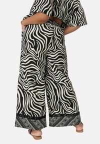 Wijdvallende broek met een zwart-wit zebra print, voorzien van een gestructureerde zoom en patroonaccenten. Gemaakt van lichtgewicht stof.