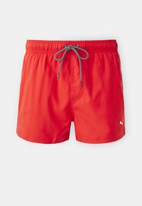 Red swim shorts with an elastic waistband, featuring a black and white drawstring and a side pocket. Logo in white on the hem.