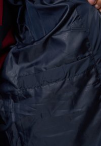 Marine binnenvoering van een jas met een gladde, glanzende textuur. Bevat een zak met een nette, horizontale naad. Subtiele branding zichtbaar.