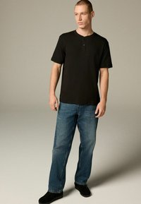 Sort kortærmet henley skjorte med to knapper, parret med blå denim jeans. Outfitet fuldendes med sorte sko.