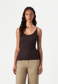 Haut sans manches marron avec un col rond, fabriqué à partir d'un tissu lisse, au design ajusté, associé à un pantalon beige.
