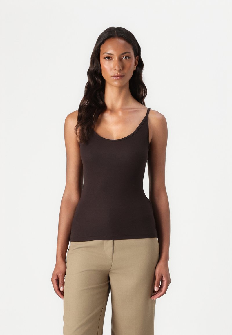 Haut sans manches marron avec un col rond, fabriqué à partir d'un tissu lisse, au design ajusté, associé à un pantalon beige.