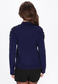 Granatowy sweter z wysokim kołnierzem i dekoracyjnymi cekinami na ramionach. Wykonany z miękkiego materiału, z dopasowanym krojem i ściągaczami na mankietach.