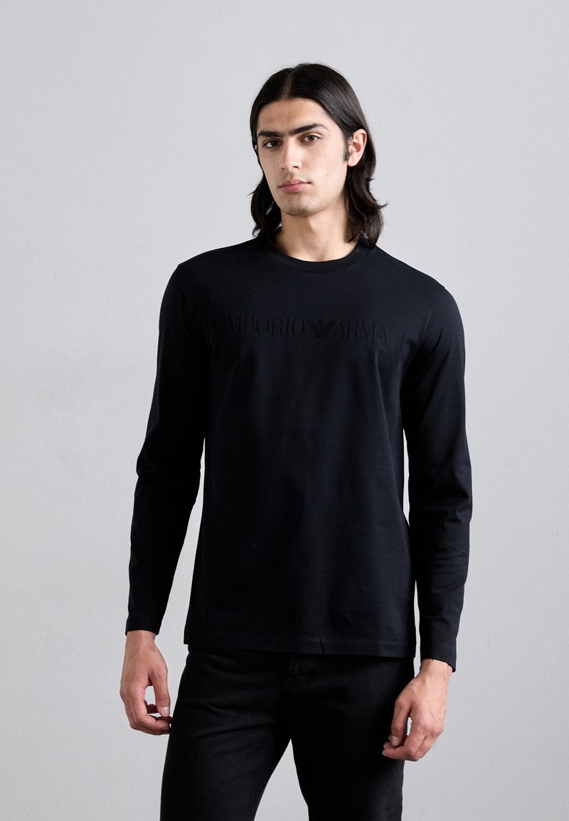 T-shirt preto de manga longa feito de tecido macio, com um logótipo tonal "Emporio Armani" impresso no peito. Design simples e clássico.