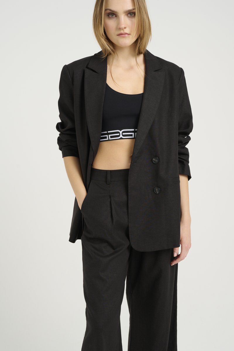 Blazer nero su misura con una vestibilità rilassata, caratterizzato da bottoni grandi e una sottile consistenza, abbinato a pantaloni a vita alta coordinati.