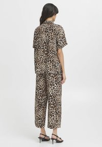 Ensemble de chemise et pantalon en imprimé léopard, fabriqué en tissu léger. Manches courtes, coupe décontractée et pantalons larges. Accents noirs sur les chaussures.