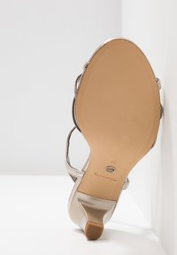 Sandale à talons pour femmes avec semelle beige et finition métallique argentée, taille 37, présentée debout contre un fond blanc en coin.