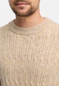 Beige kaapokkevit swetari, ihe round neckline, nwere usoro nwere ụcha na ribbed cuffs, emegharịrị site na ihe dị nro, na-ekpo ọkụ.