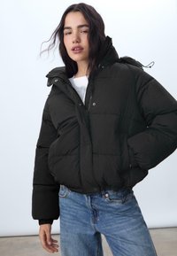 Giubbotto imbottito nero con zip frontale, bottoni a pressione e colletto alto. Presenta tasche laterali e un design testurizzato, trapuntato.