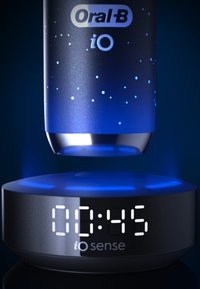 Brosse à dents électrique Oral-B iO avec un manche noir texturé et des accents bleus illuminés ; la base de chargement affiche un minuteur au format numérique blanc.