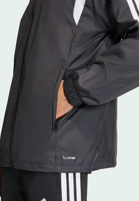 Μαύρο μπουφάν με φερμουάρ, ελαστικούς καρπούς, πλαϊνές τσέπες και λευκές ρίγες στους ώμους. Ορατό λογότυπο CLIMA 365.