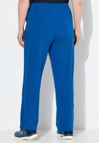 Blå, lätta, elastiska midjebyxor med raka ben, kombinerat med mörka träningsskor. Slät textur utan synliga mönster eller detaljer.