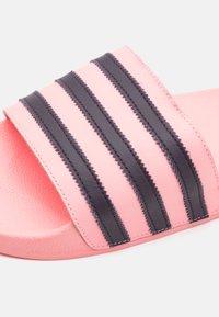 Ružová šlapka s textúrovaným popruhom, ktorý má tri horizontálne čierne pruhy. Podrážka je hladká a mierne kontúrovaná.