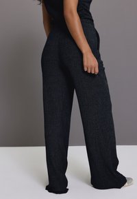 Pantaloni a gamba larga neri con tessuto testurizzato, caratterizzati da una vestibilità ampia e dettagli discreti. Caratterizzati da una cintura in vita e una tasca laterale.