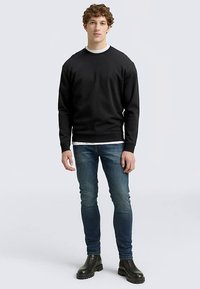 Bluză neagră cu guler rotund, cu croială lejeră, purtată peste un tricou alb, combinată cu blugi albaștri și cizme negre până la gleznă.