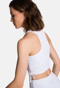Witte geribbelde crop top met verstelbare zijkanten, ronde halslijn en brede schouderbanden. Gladde textuur, nauwsluitend ontwerp voor actieve kleding.