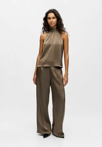 Khaki Satin-Haltertop kombiniert mit weit geschnittenen Hosen; glatte Textur, minimalistisches Design und subtiler Glanz. Ergänzt durch Stiefeletten.