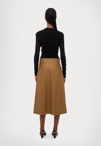 Mustat pitkät hiharat, joissa on kootut tekstuurit, yhdistettynä vaaleanruskeaan, polvipituiseen hameeseen. Asusteessa on sileä pinta ja vähäiset saumat.