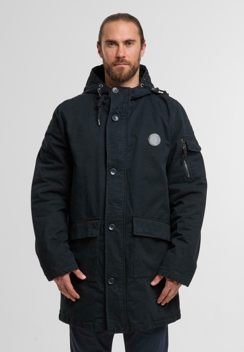 Black hooded parka made of sturdy fabric. Features large front pockets, button closure, drawstring hood, and a zippered pocket on the sleeve.