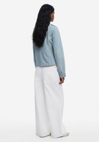 Svijetloplava prugasta traper jakna s dugim rukavima, stražnjim džepovima i skraćenim dizajnom, uparen s širokim bijelim hlačama i svijetlim obućom.