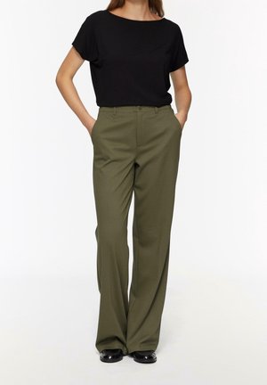 Černý krátký rukávový top kombinovaný s vysokými olivově zelenými kalhotami. Kalhoty mají boční kapsy a rovný střih nohavic. Černá obuv.