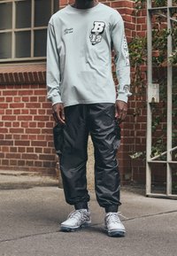 Helles blaues Langarmshirt mit grafischen Drucken, kombiniert mit schwarzen Cargo-Hosen mit Taschen und elastischen Bündchen. Graue Sportschuhe.
