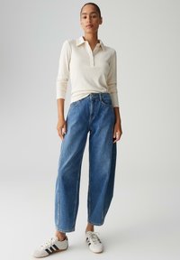 Polo a maniche lunghe a coste color beige chiaro abbinata a jeans a vita alta con gamba larga blu e sneaker bianche con strisce nere.