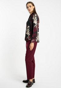 Luźna czarna bluzka z kwiatowymi wzorami w odcieniach beżu i burgundowym, w zestawie z burgundowymi spodniami o dopasowanym kroju oraz błyszczącymi czarnymi loaferami. Gładka tekstura.