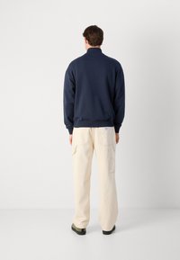 Sudadera navy con cuello alto, puños y dobladillo acanalados; combinada con pantalones cargo crema que cuentan con bolsillos laterales y un ajuste relajado.