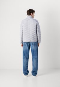 Lichtgrijze pufferjack met een gewatteerde textuur, hoge kraag en getailleerde pasvorm, gecombineerd met relax-fit blauwe jeans.