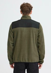 Giacca in pile verde con pannello in nylon nero sulla parte superiore della schiena, colletto con zip e cuciture piatte. Texture morbida e vestibilità rilassata per il comfort.