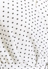 Tissu blanc avec un motif de petits points noirs. La texture semble douce et légère, adaptée à des vêtements décontractés.