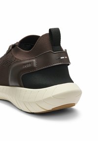 Sneaker marrone in mesh con tallone texturizzato nero, suola color crema con motivo antiscivolo e linguetta posteriore.