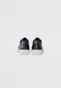 Baskets en cuir bleu marine foncé avec une finition texturée, semelle en caoutchouc blanc et arrière arrondi, présentant des éléments de design minimalistes.