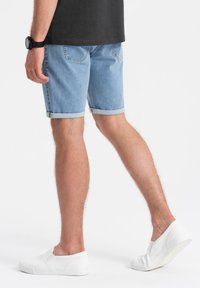 Shorts de mezclilla azul claro con dobladillos enrollados, bolsillos traseros y una textura ligera. Se lleva con zapatos blancos de lona y una camiseta oscura.