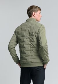 Olijf groene pufferjack heeft een gestikt ontwerp, een staande kraag en smal gesneden mouwen met ribbels aan de manchetten en onderkant.