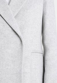 Cappotto grigio in misto lana con un motivo a spina di pesce testurizzato, rever a punta e tasca laterale, con una finitura liscia.