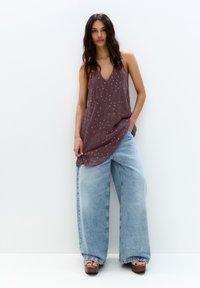 Top violet fără mâneci cu modele albe în buline, asortat cu pantaloni lejeri din denim albastru cu picioare largi și sandale cu platformă maro.