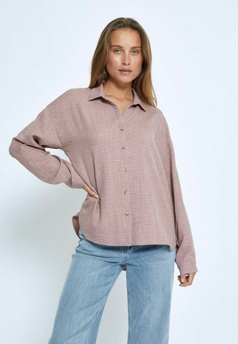 Light pink long-sleeve shirt in textured fabric with a button-down front, collar, and relaxed fit, paired with light blue jeans.